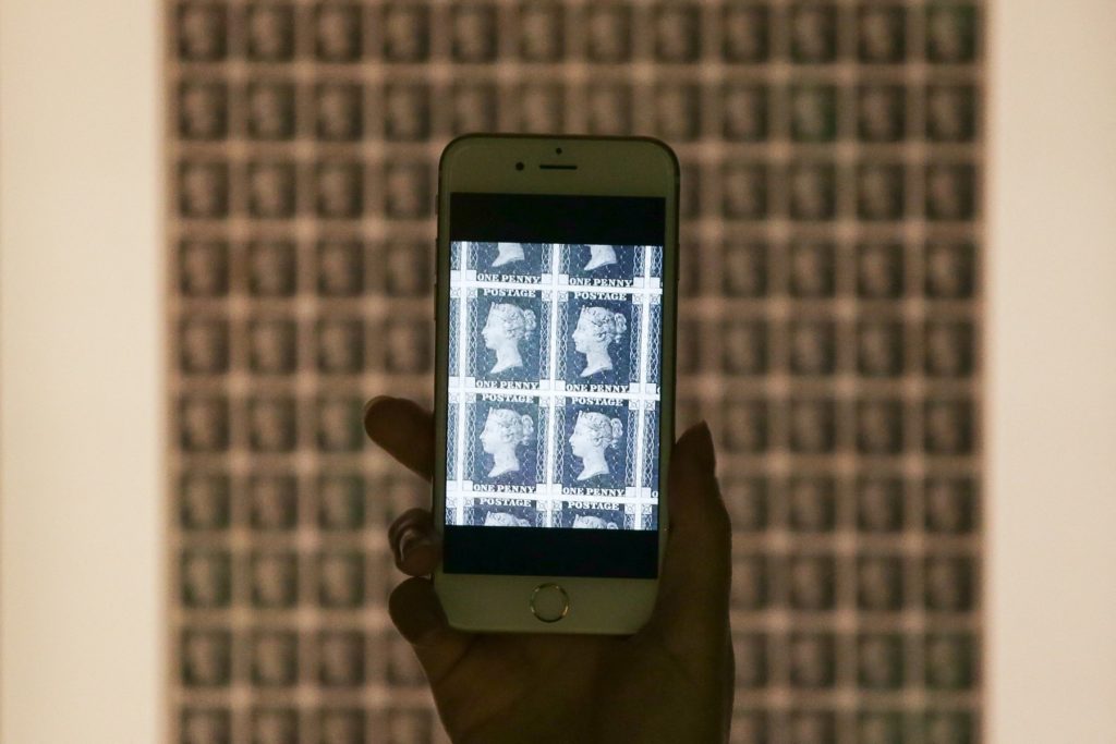 An organiser holds a smartphone in front a complete sheet of Penny Black stamps, generally acknowledged as the world's first postage stamp, during a media preview of the new Postal Museum and the Mail Rail attraction in London on July 26, 2017. Snaking through special underground tunnels that have lain abandoned for years, London's Mail Rail is opening to the public for the first time for a ride on tiny trains that not even the Blitz could stop. The attraction is part of the new Postal Museum opening on July 28 that retraces the vital role Britain's Royal Mail played over its 500 year history.,Image: 343257527, License: Rights-managed, Restrictions: EMBARGOED AND NOT FOR USE UNTIL 0001GMT JULY 28, 2017 - THIS EMBRAGO INCLUDES ONLINE USE, Model Release: no